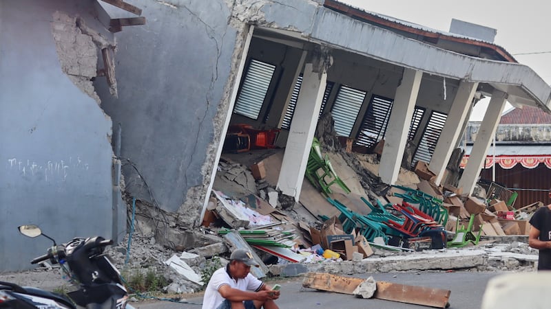 A man checks his phone near a building collapsed due to an earthquake, in Reok, East Nusa...