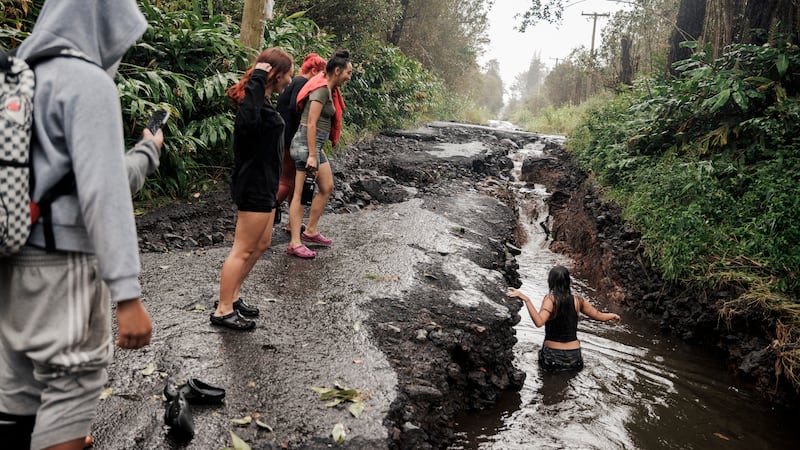 A teenager wades through a pool of water in a washed-out section of a damaged road in Mountain...