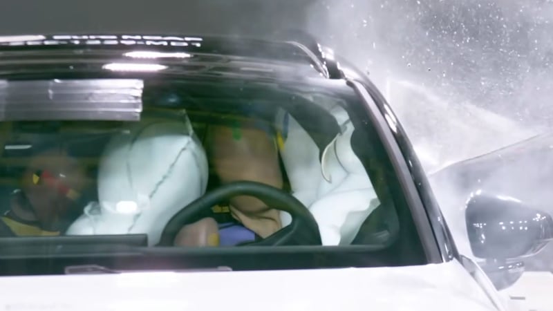 Two crash test dummies are seen in a vehicle being hit on the driver's side. White airbags are...